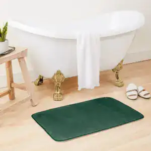 Flaschengrüne Badematte vor Badewanne mit goldfarbenen Füßen, stilvolles Badezimmer.