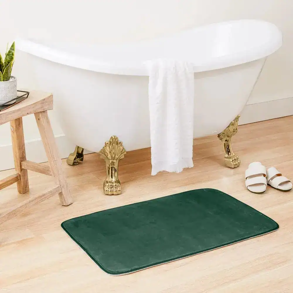 Flaschengrüne Badematte vor Badewanne mit goldfarbenen Füßen, stilvolles Badezimmer.