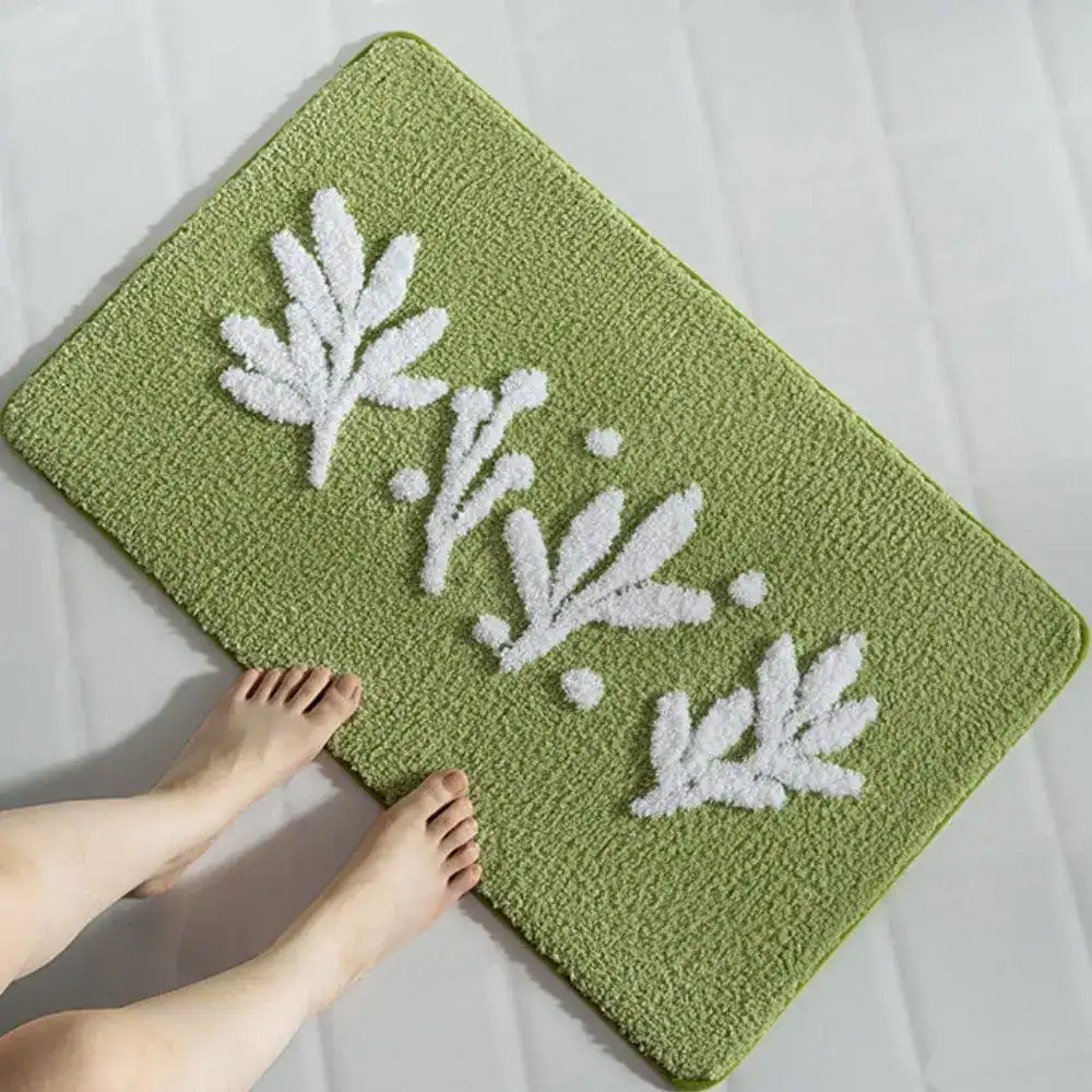 Olivgrüne Badematte mit weißen Blattmotiven, Fuß darauf, für Komfort und Stil im Badezimmer.