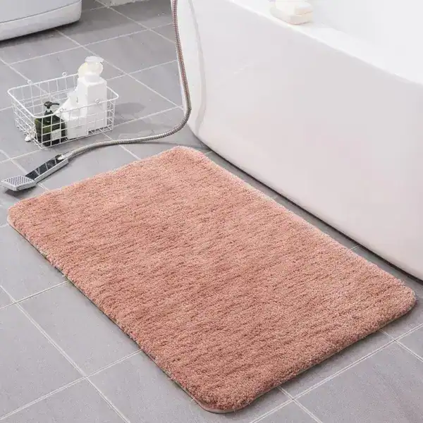 Weicher Badezimmerteppich in Rosa vor Badewanne auf Fliesenboden.