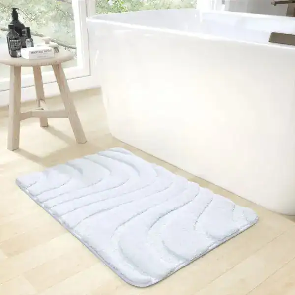 Weißer Badezimmerteppich mit Wellenmuster vor Badewanne.