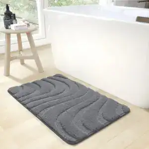 Dunkelgrauer Badteppich mit wellenförmigem Design vor weißer Badewanne.
