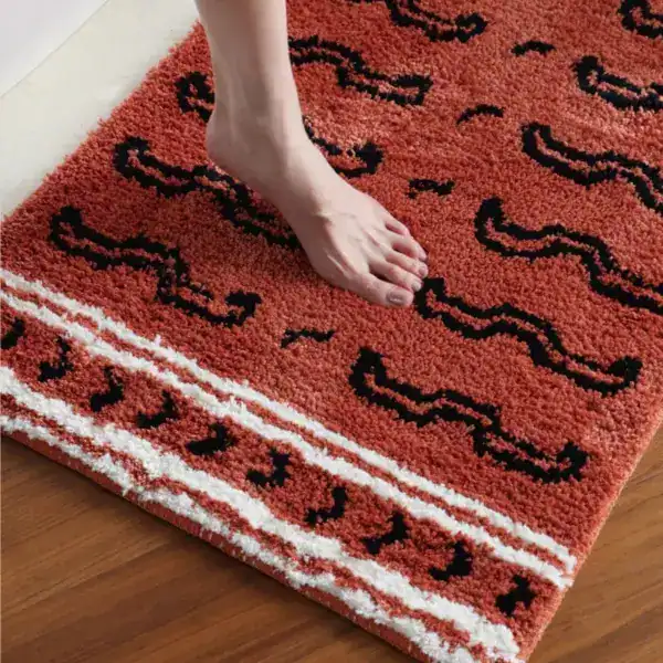 Gemusterter Badteppich in Orange mit schwarzen und weißen Mustern, Fuß darauf.