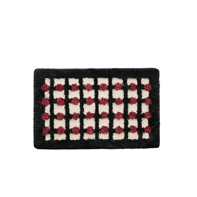 Geometrische Badematte mit schwarzer und cremefarbener Karomusterung und roten Pompons.