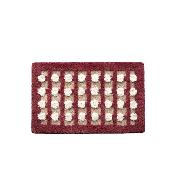 Geometrische Badematte mit weißen Pompons und bordeauxrotem Rand.