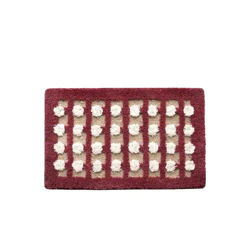 Geometrische Badematte mit weißen Pompons und bordeauxrotem Rand.