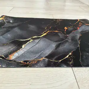 Badematte in Schwarz mit goldener Äderung auf hellem Holzboden